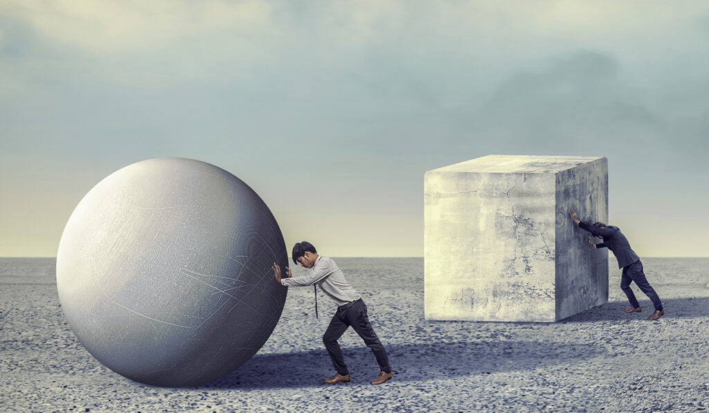 Man pushing sphere and cube in barren landscape