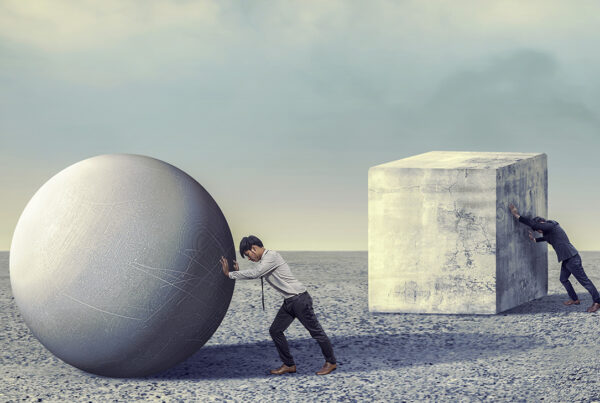 Man pushing sphere and cube in barren landscape